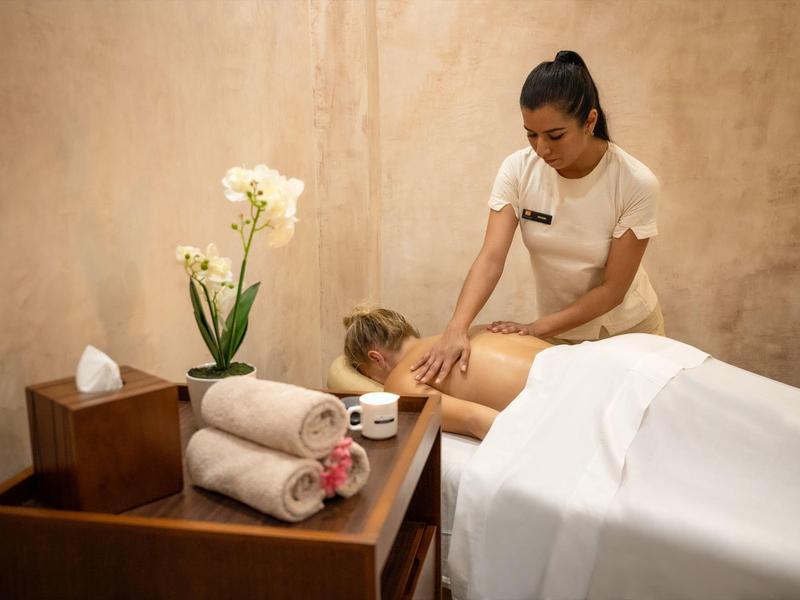 Woman receiving a back massage in a serene spa room with towels and orchids nearby.