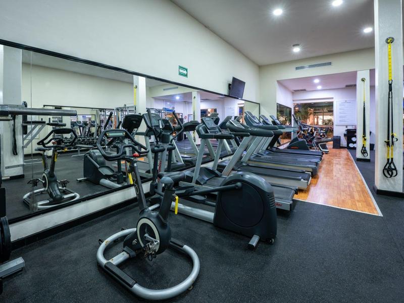 Modern gym with treadmills, exercise bikes, and mirrored wall in a hotel or fitness center.