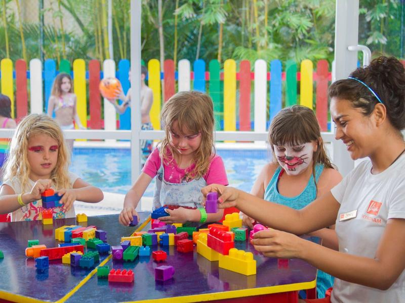 Children and a woman playing with colorful building blocks at a table in a bright room.