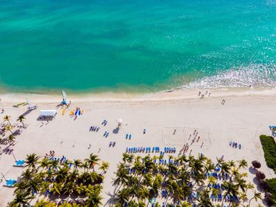 Strand mit weißem Sand, blauer Lagune, Palmen und verstreuten Liegestühlen bei sonnigem Wetter.