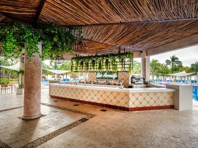 Offene Bar mit Bambusdach, grünem Pflanzenbehang und Pool im sonnigen Außenbereich.