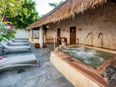 Außenbereich mit Jacuzzi, Liegestühlen und einem strohgedeckten Gebäude im tropischen Garten.