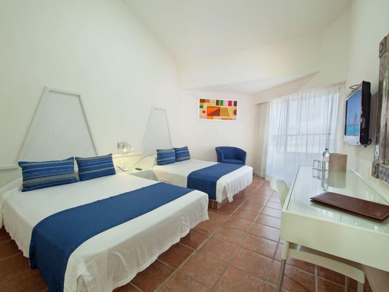 Hell eingerichtetes Schlafzimmer mit zwei großen Betten, blauen Decken und Kachelfußboden.