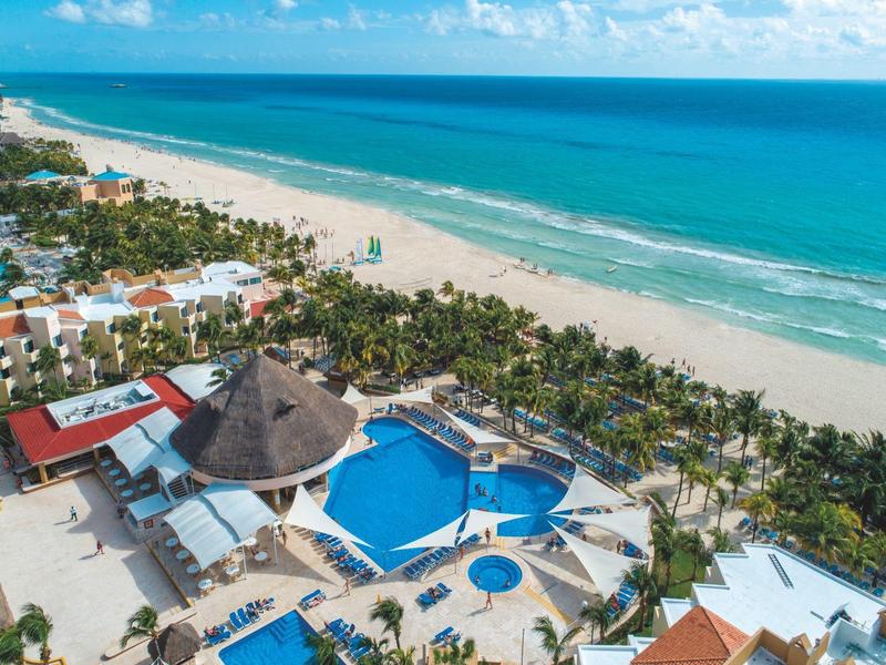 Luftaufnahme eines tropischen Resorts mit Pool, Palmen und weitem Sandstrand am türkisfarbenen Meer.