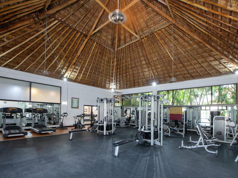 Weitläufiges Fitnessstudio mit Holzdach, großen Fenstern und vielseitigen Trainingsgeräten.