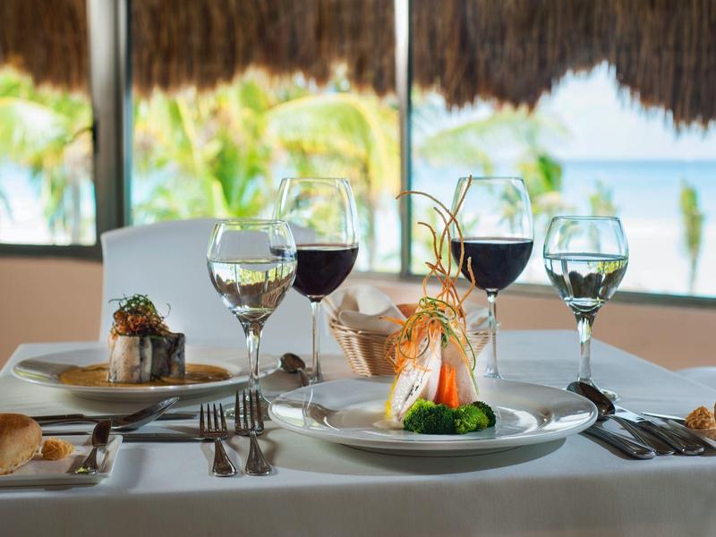 Elegantes gedeckter Tisch mit Wein und Fischgericht vor offenem Fenster und Meeresblick.