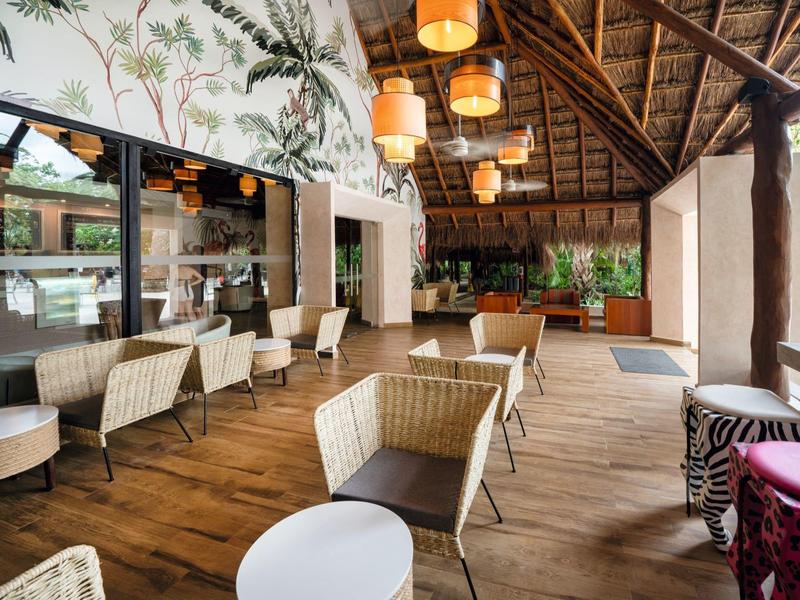Offener, tropisch dekorierter Sitzbereich mit Holzboden, Rattanmöbeln und hängenden Lampen.