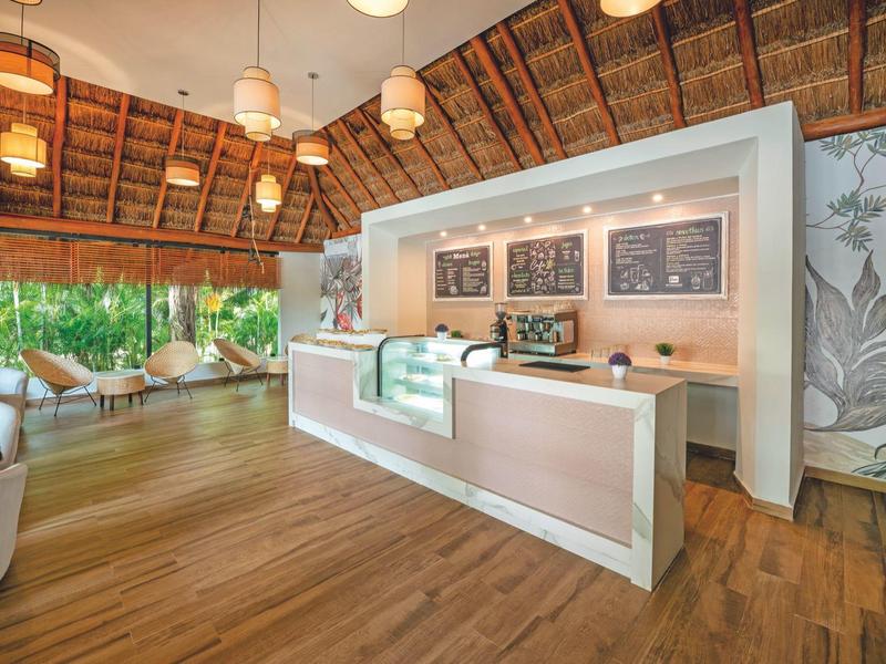 Helle Rezeption mit Holzfußboden, hohen Decken und modernen Lampen in tropischer Umgebung.