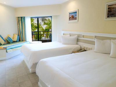 Hotel room with two white beds and a balcony view of palm trees.