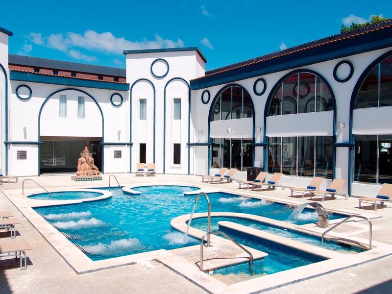 Piscina all'aperto moderna in un hotel elegante con facciata bianca e cielo blu.