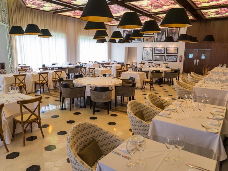 Ristorante elegante con tavoli apparecchiati, sedie con motivo e lampadari neri.
