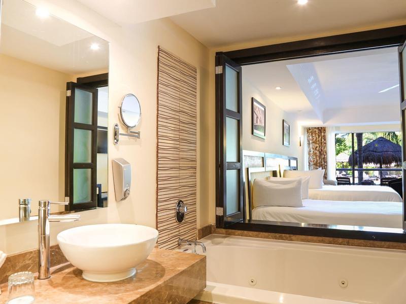 Area bagno moderna in hotel con lavabo, grande specchio e vasca da bagno con vista sul soggiorno.