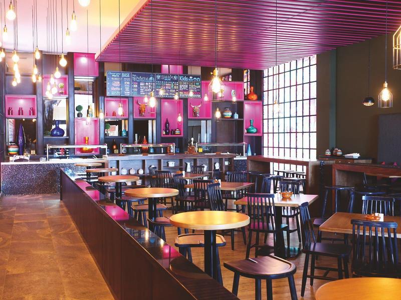 Area bar dell'hotel moderna con tavoli rotondi, sedie, illuminazione calda e arredi neri.