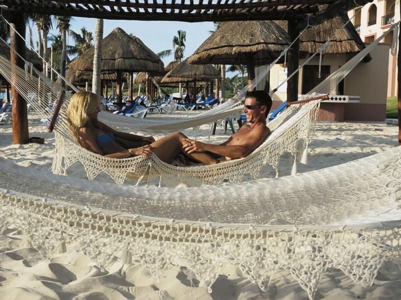 Due persone si rilassano insieme in amache sulla spiaggia di un hotel.