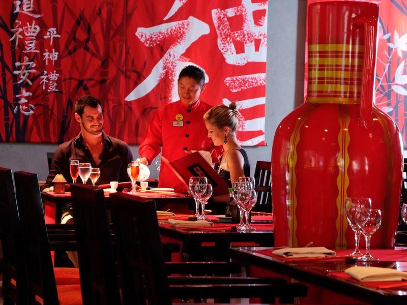 Due ospiti seduti a un tavolo serviti da un cameriere in un ristorante a tema asiatico.