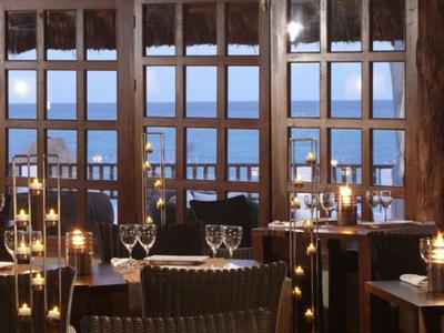 Restaurant mit Holzbalken, Kerzenlicht und Blick auf das Meer durch große Fenster.