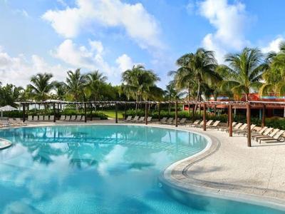 Großer Poolbereich mit Palmen, Liegestühlen und sonnigem Himmel in einem tropischen Resort.