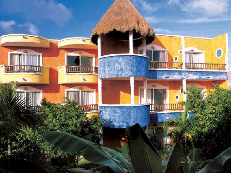 Edificio dell'hotel colorato con balconi circondato da piante tropicali lussureggianti e cielo azzurro.