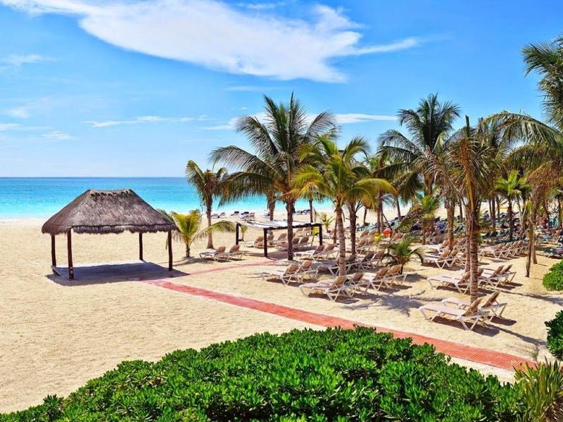 Spiaggia soleggiata con palme, lettini e una piccola capanna di paglia vicino al mare azzurro.