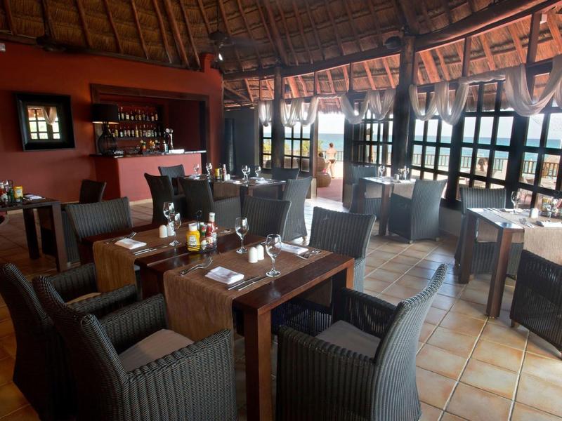 Accogliente ristorante con tavoli in legno, sedie imbottite, pavimento piastrellato e grande finestra per luce naturale.