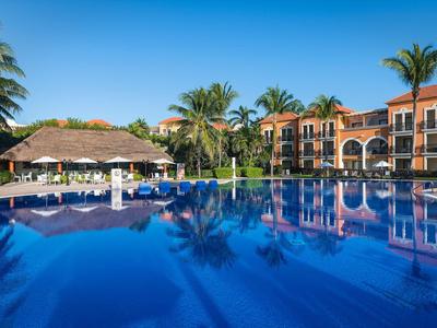 Grande piscina con superficie d'acqua blu davanti a edifici dell'hotel e palme sotto un cielo limpido.