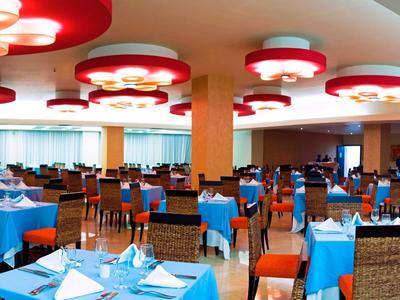 Ampia sala da pranzo dell'hotel con tovaglie blu, tavoli e sedie disposti ordinatamente sotto luci rosse.