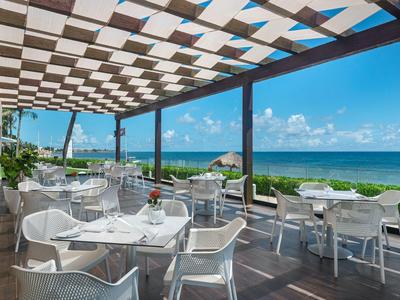 Terrazza con sedie e tavoli bianchi con vista sul mare sotto un cielo soleggiato.