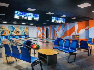 Moderna pista da bowling con quattro corsie, sedili blu e design murale arancione-blu brillante.