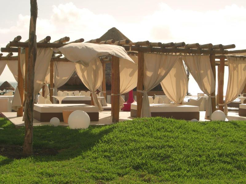 Area lounge esterna con pergolati in legno e tende bianche su una collina erbosa.