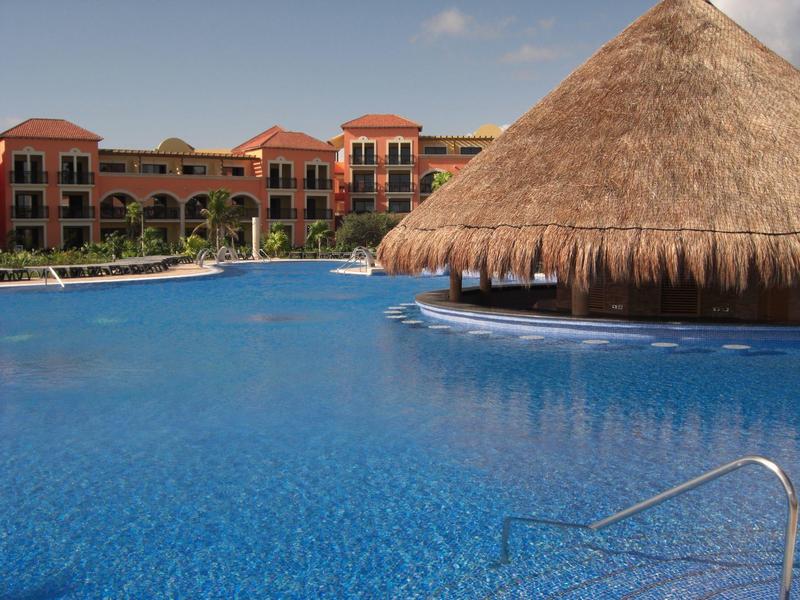 Piscina resort con bar di paglia e edificio a più piani sotto cielo sereno.