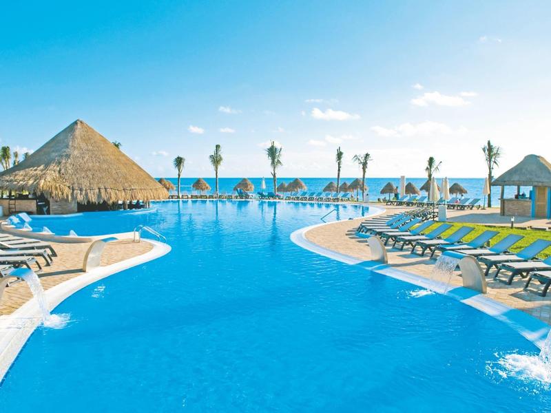 Grande piscina all'aperto con lettini e ombrelloni di paglia vicino a un oceano limpido.