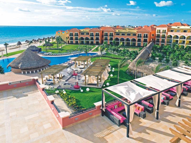 Resort sulla spiaggia con piscina, lettini e vista sull'oceano sotto un cielo limpido.