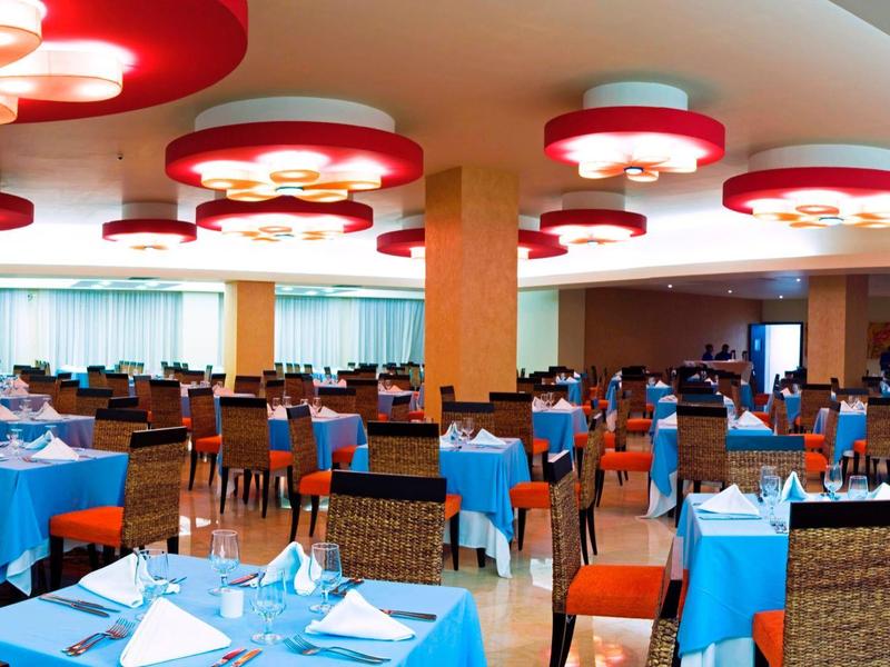 Ampia sala da pranzo dell'hotel con tovaglie blu, tavoli e sedie disposti ordinatamente sotto luci rosse.