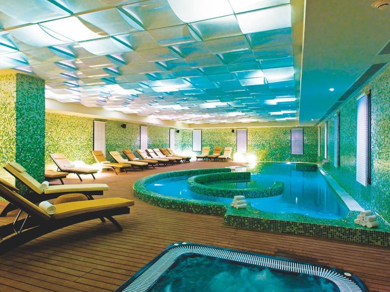 Area piscina interna con lettini e illuminazione calda in una spa o hotel moderno.