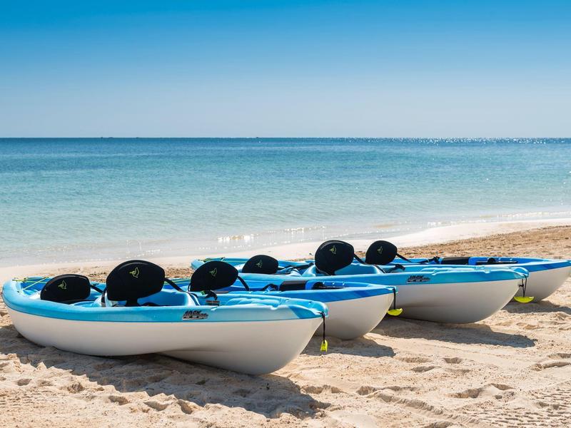 Tre kayak blu su una spiaggia sabbiosa vicino al mare calmo sotto un cielo sereno.