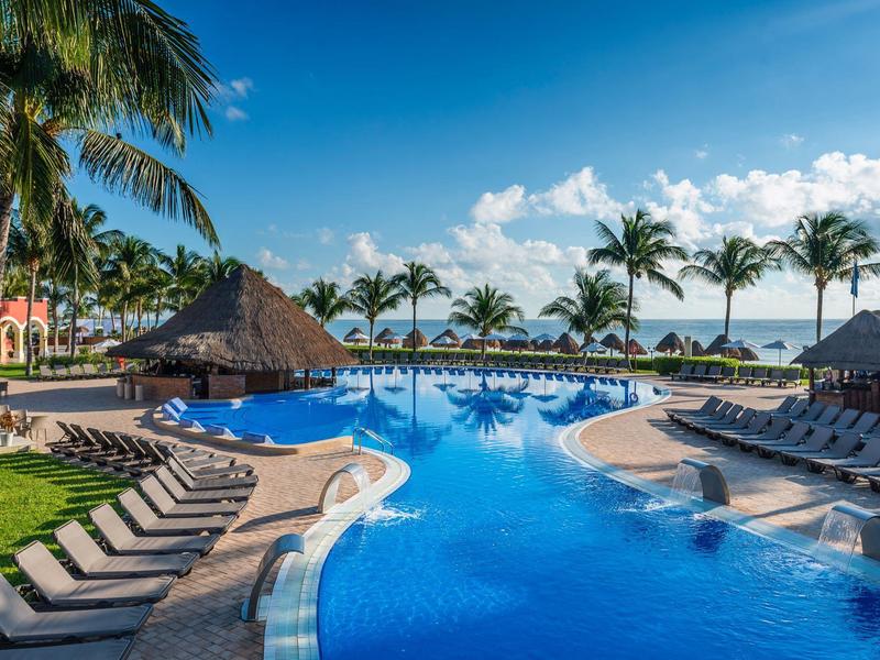 Piscina del resort con lettini, palme e cielo azzurro vicino alla spiaggia.