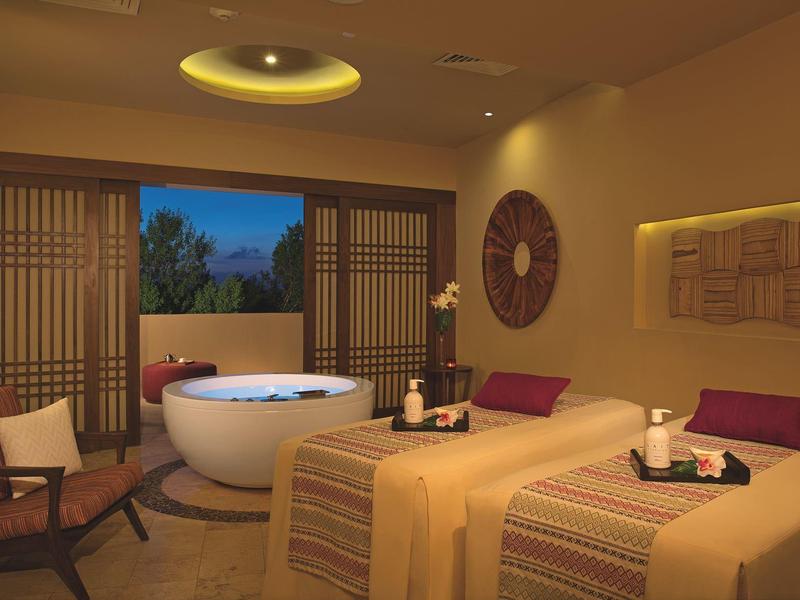 Accogliente stanza spa con lettini da massaggio, vasca rotonda, illuminazione calda e porte scorrevoli verso l'esterno.