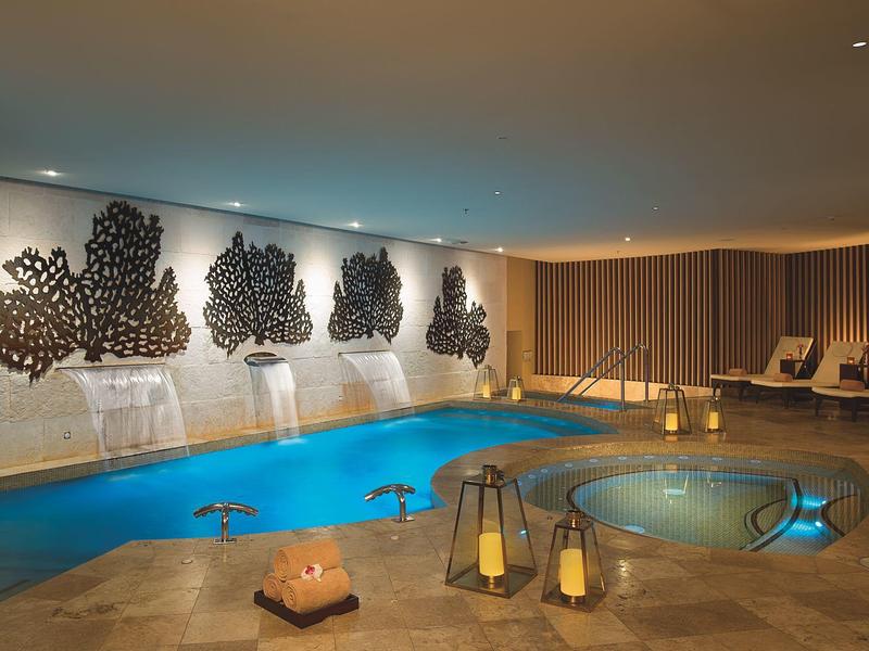 Area piscina interna con lettini, decorazioni murali e illuminazione soffusa per un'atmosfera rilassante.