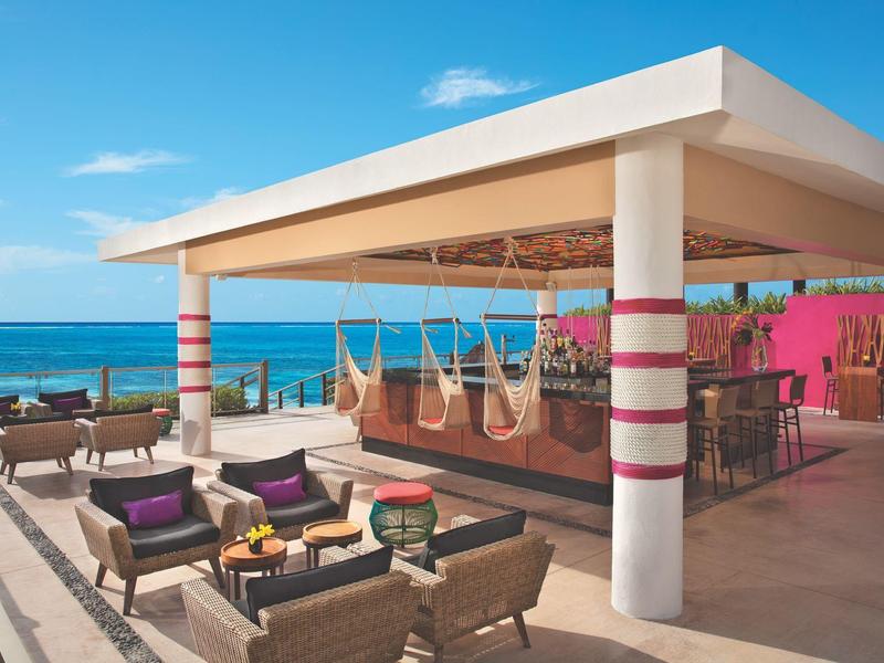 Bar sulla spiaggia all'aperto con zone lounge e vista sull'oceano sotto un cielo limpido.