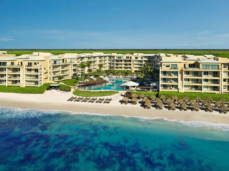 Grande resort fronte mare con piscine, lettini e acque oceaniche blu sotto un cielo limpido.
