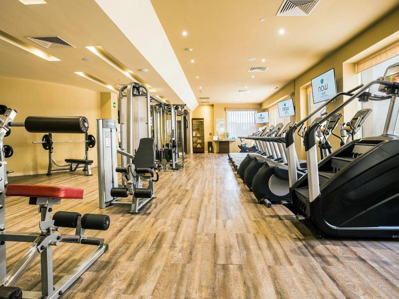 Palestra moderna dell'hotel con macchine cardio e pesi su pavimento in legno con illuminazione.