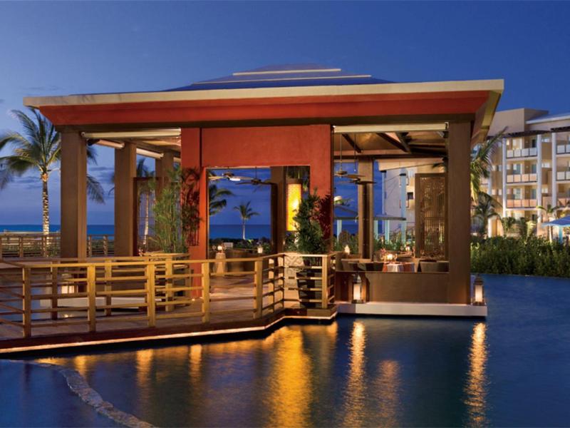 Elegante padiglione a bordo piscina con illuminazione calda e sfondo tropicale al crepuscolo.