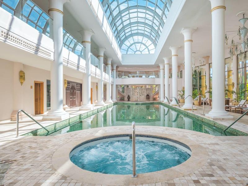 Piscina interna con vasca idromassaggio e tetto in vetro in un'area hotel luminosa.