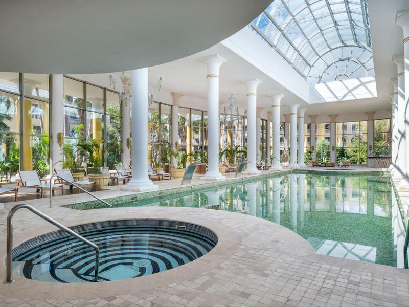 Piscina interna con vasca idromassaggio in un moderno hotel benessere con grandi finestre e colonne.