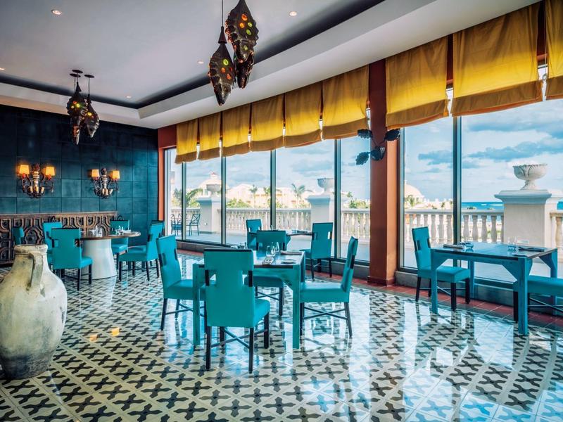 Ristorante dell'hotel con sedie turchesi, grandi finestre e vista sul mare alla luce del giorno.