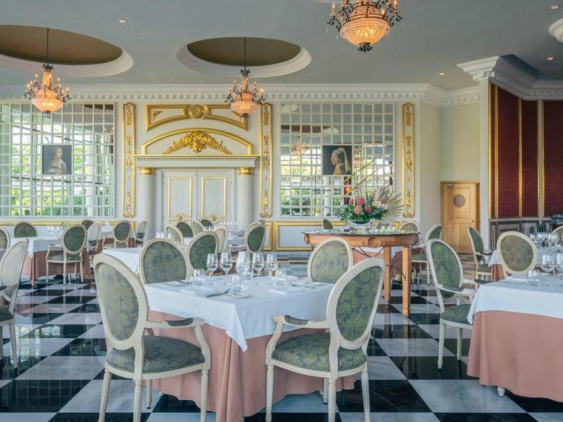 Sala da pranzo elegante con pareti bianche, tavoli rotondi e sedie verdi imbottite.