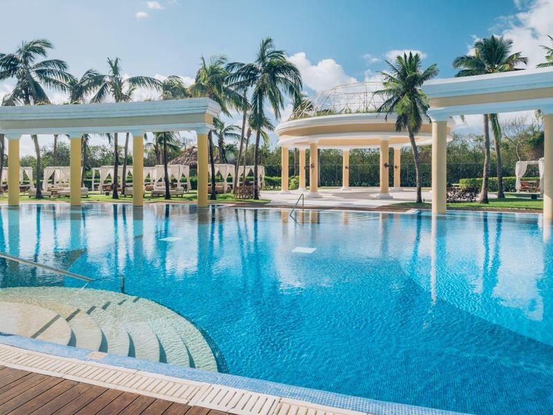 Grande piscina blu con palme e padiglioni bianchi in un resort tropicale.
