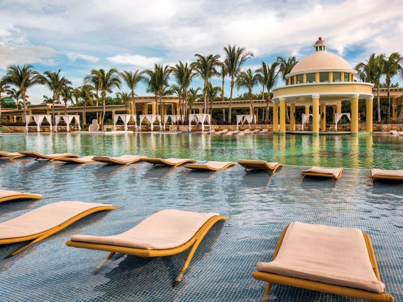 Area piscina di lusso con lettini e palme in un resort hotel sotto un cielo nuvoloso.