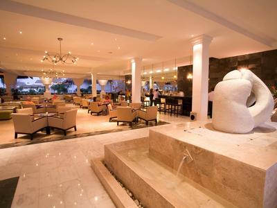 Lobby d'hotel luminosa ed elegante con marmo, sculture e zone salotto accoglienti.