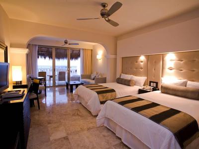 Camera d'hotel moderna con due letti grandi, scrivania, TV e balcone con vista esterna.